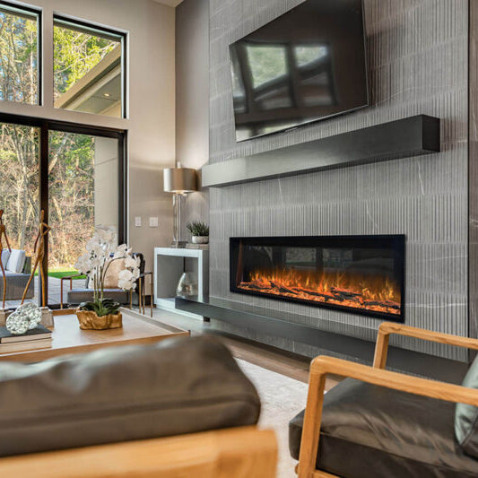 Modern living room with a linear electric fireplace built into a gray tile wall beneath a wall-mounted TV, with floor-to-ceiling windows overlooking trees