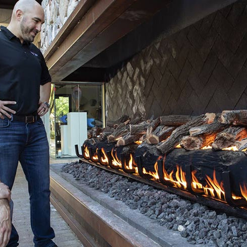 Two installers inspecting a lit Grand Canyon gas log set in an outdoor stone fireplace